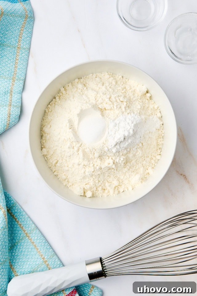 Overhead view of flour, baking powder, and salt in a white bowl, ready to be whisked together.