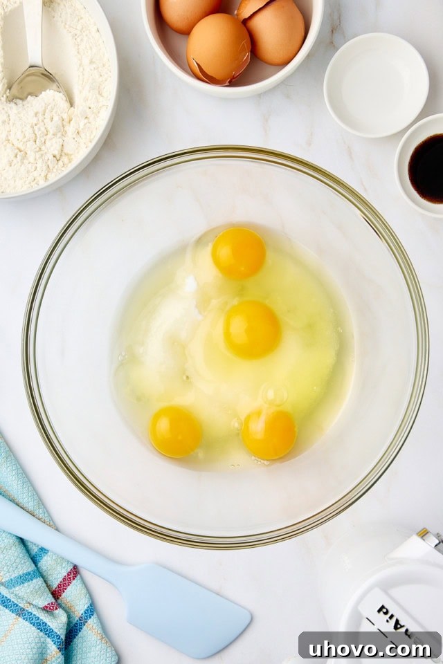 Overhead view of sugar and eggs in a glass mixing bowl, beaten until pale and fluffy.