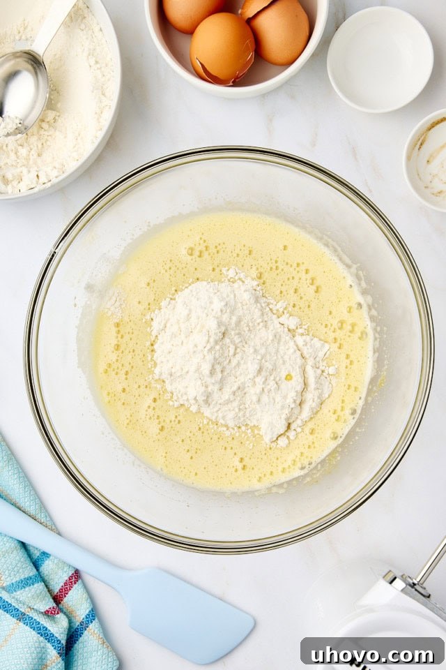 Overhead view of dry ingredients being gradually added to beaten eggs and sugar in a mixing bowl.