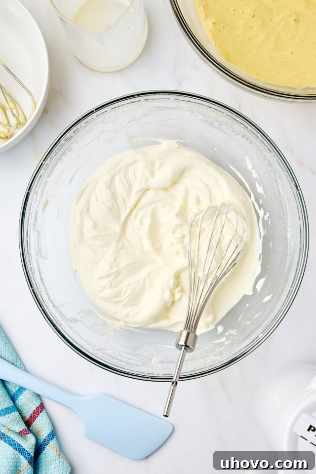 Overhead view of heavy cream whipped to soft peaks in a glass mixing bowl.
