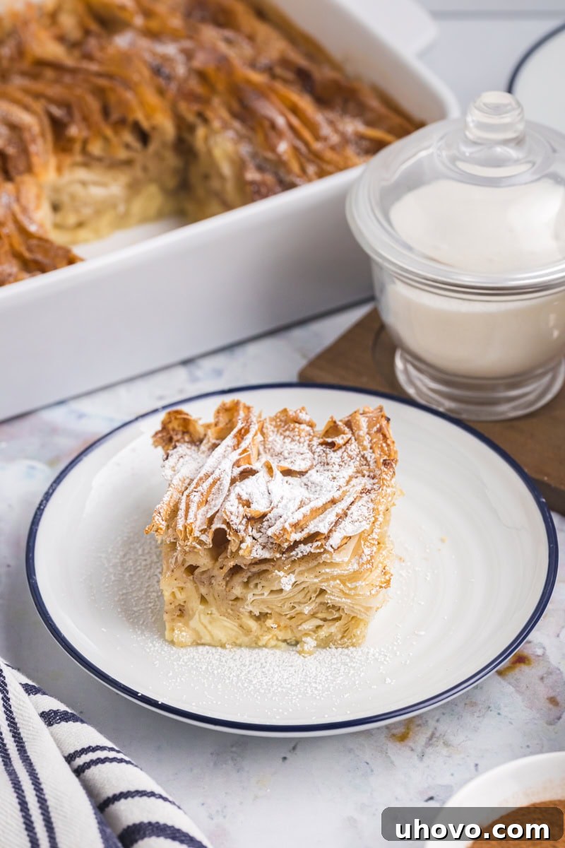 A beautifully presented slice of crinkle cake dusted with confectioners' sugar, with the remaining golden cake visible in the background.