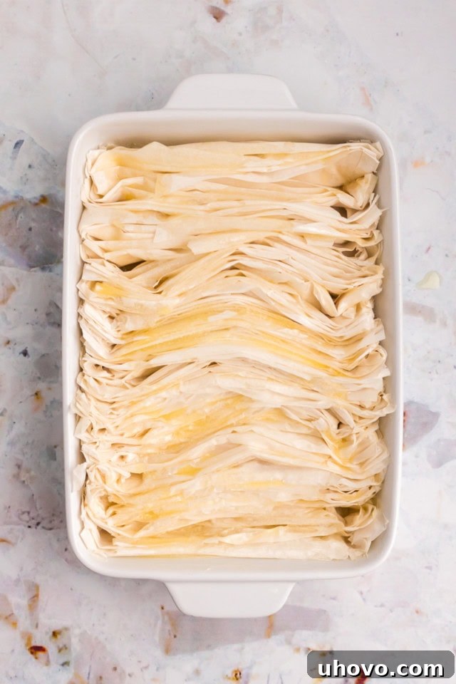 Several sheets of folded phyllo dough neatly arranged in a rectangular baking pan, glistening with melted butter.