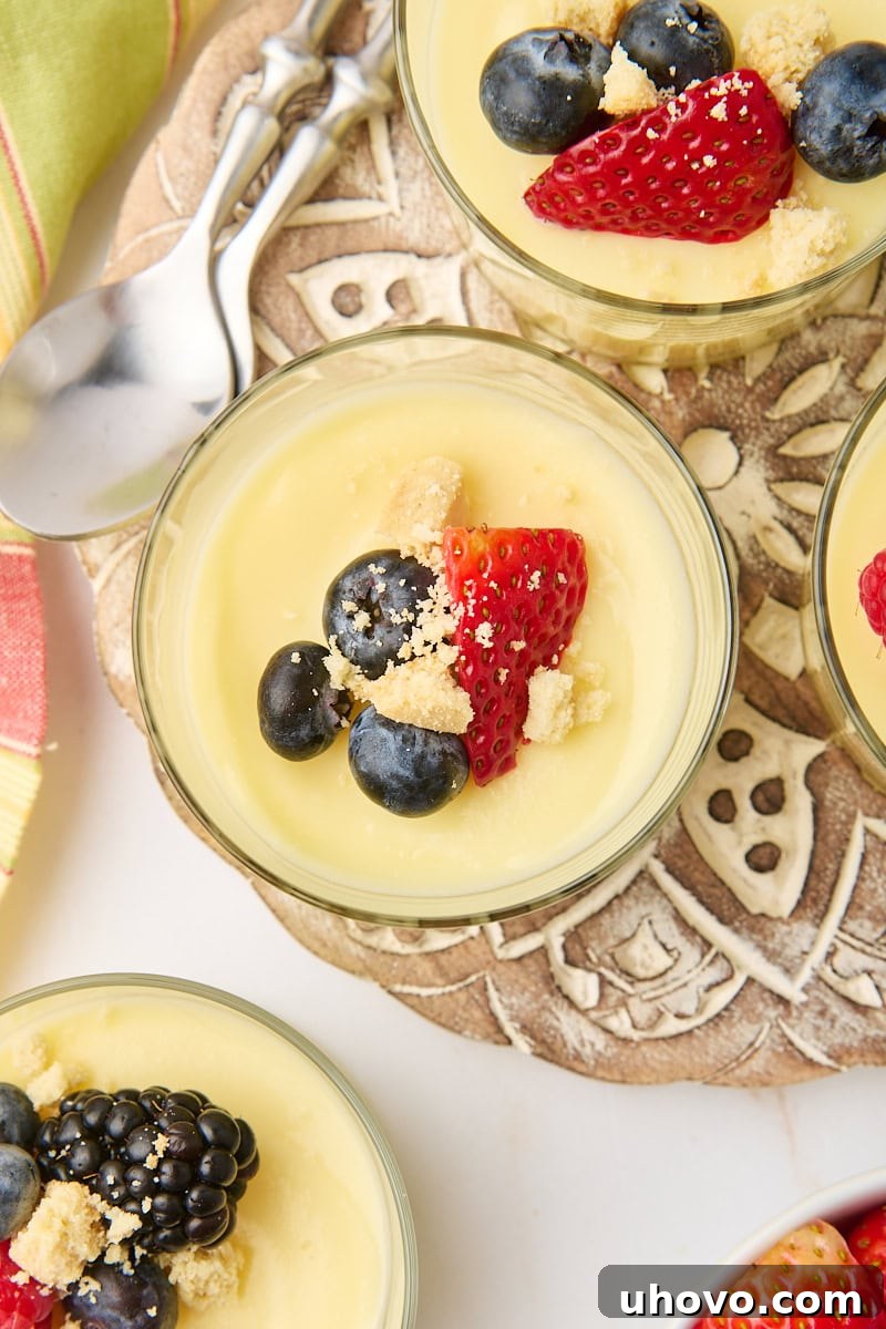 Overhead shot of multiple servings of lemon posset, beautifully presented in clear glasses and adorned with a vibrant medley of fresh berries and crushed shortbread, ready to be enjoyed as an elegant dessert.