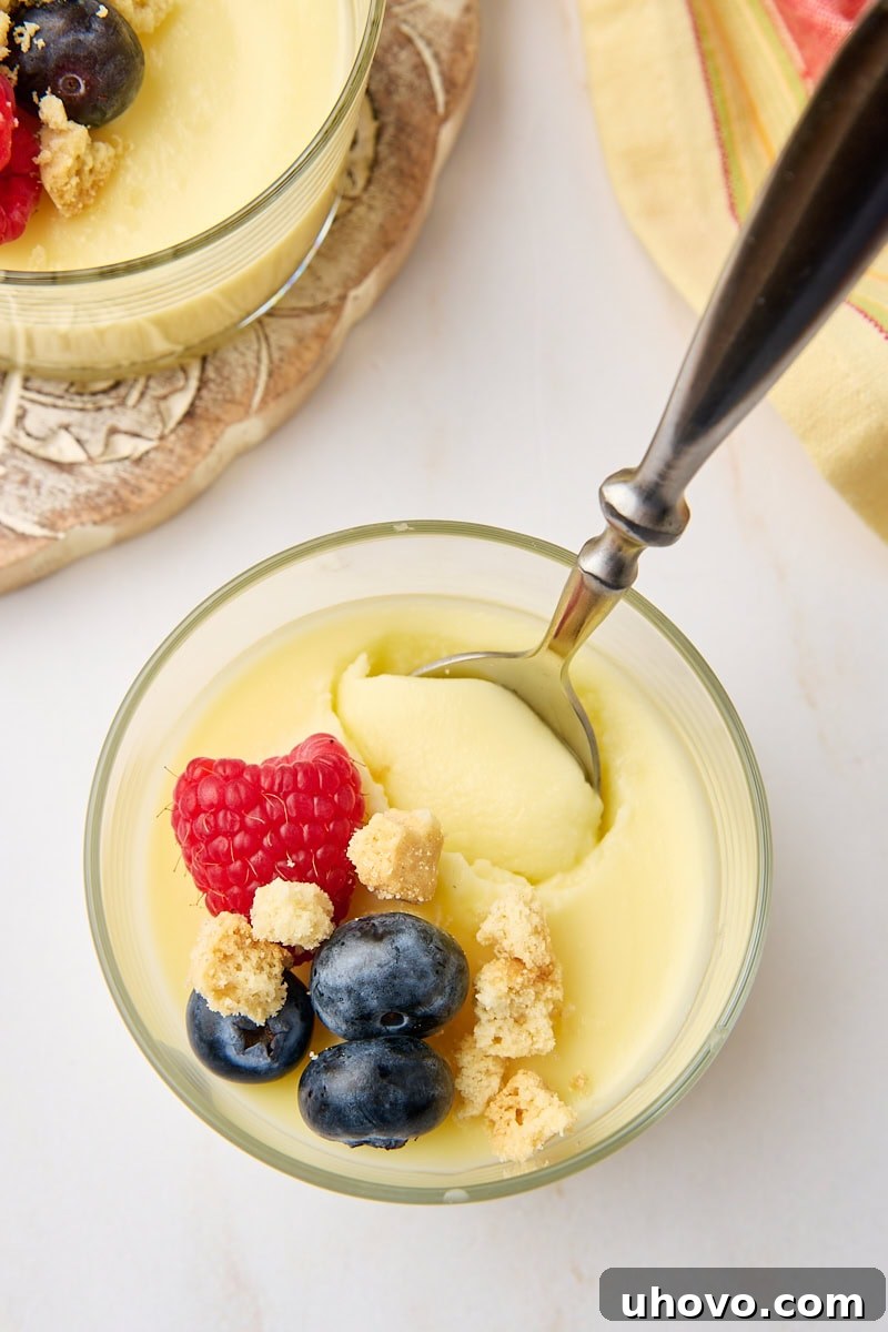 An intimate overhead shot of a lemon posset served in a clear glass, with a spoon gently scooping into the perfectly set, creamy dessert, highlighting its inviting texture.