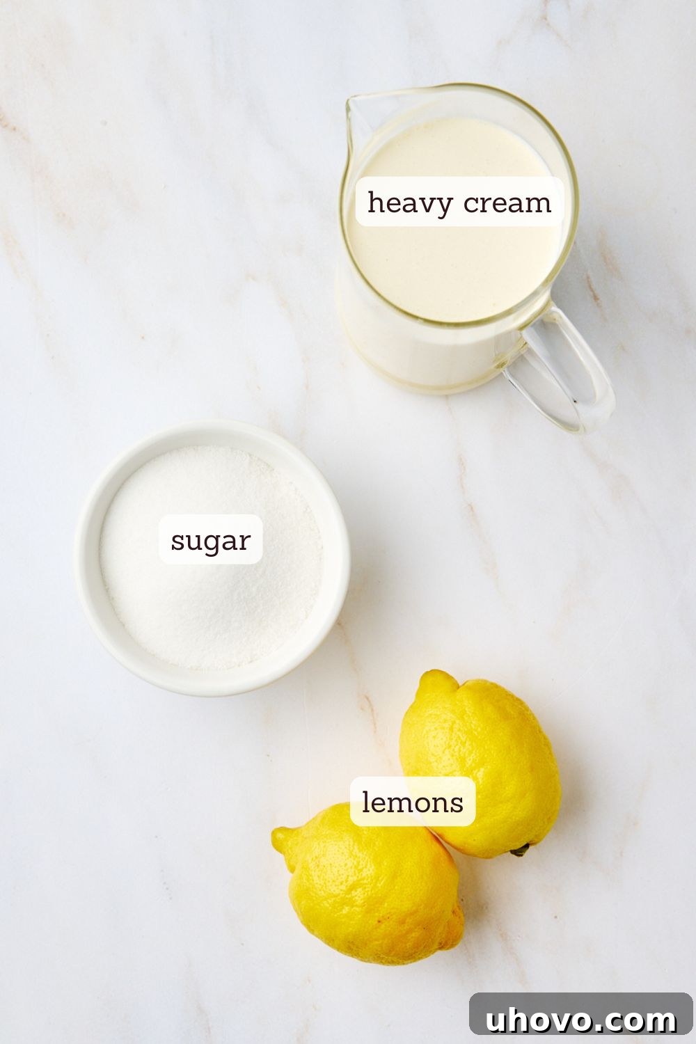 Overhead view showcasing the essential ingredients for lemon posset: a bowl of heavy cream, a bowl of granulated sugar, and several fresh, bright yellow lemons, ready for zest and juice, arranged on a rustic wooden surface.