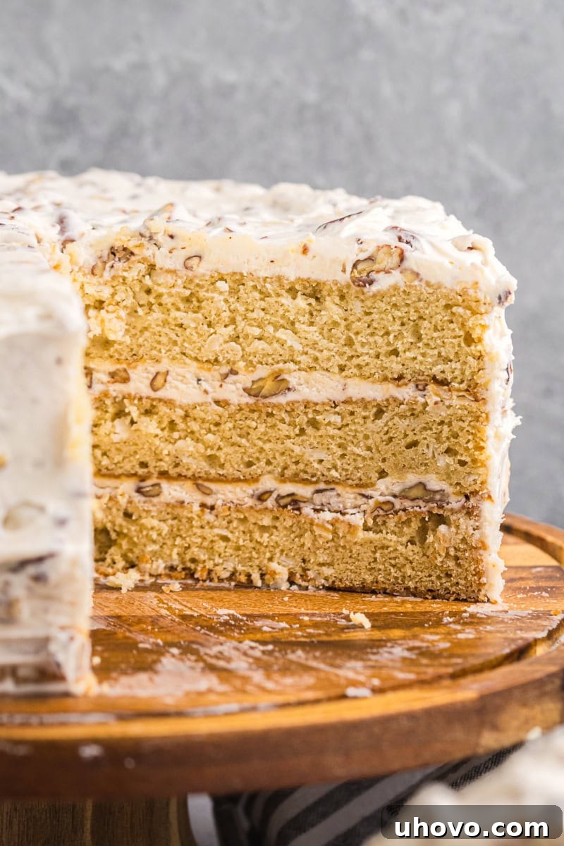A perfectly sliced Italian cream cake revealing three golden layers, rich cream cheese frosting, and visible coconut and pecans, resting on a wooden cake stand.