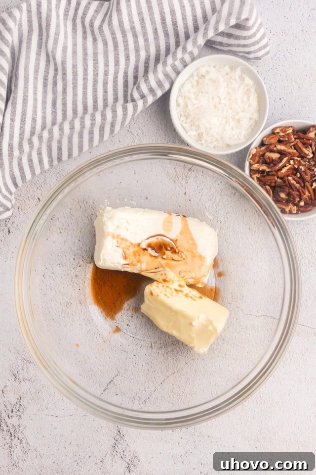 Overhead view of cream cheese, butter, and vanilla extract in a glass mixing bowl, poised for whipping into frosting.