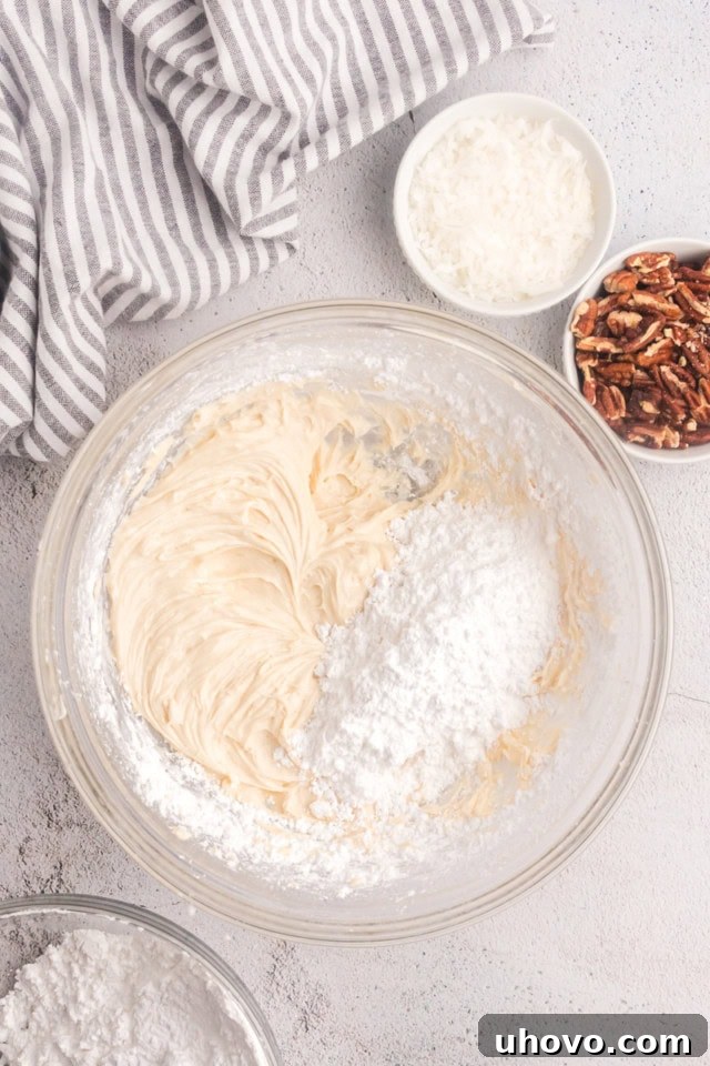 Overhead shot of confectioners' sugar being gradually added to the creamed butter and cream cheese mixture in a mixing bowl.