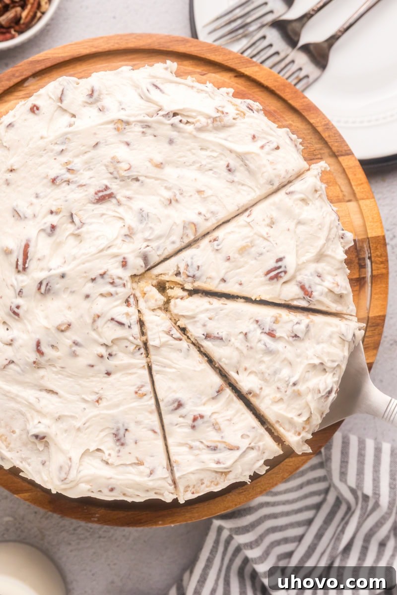 An overhead view of a partially sliced Italian cream cake, beautifully frosted and adorned with pecans, on a rustic wooden cake stand.
