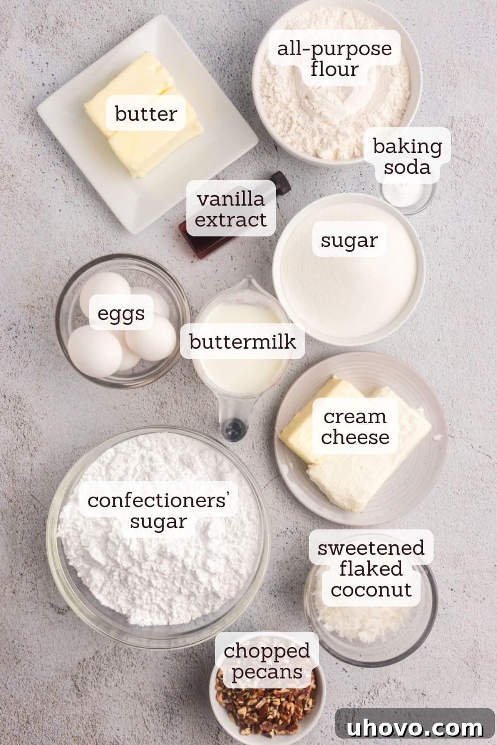 Overhead view of various Italian cream cake ingredients neatly arranged on a rustic wooden surface, including flour, sugar, butter, buttermilk, eggs, coconut, and pecans.
