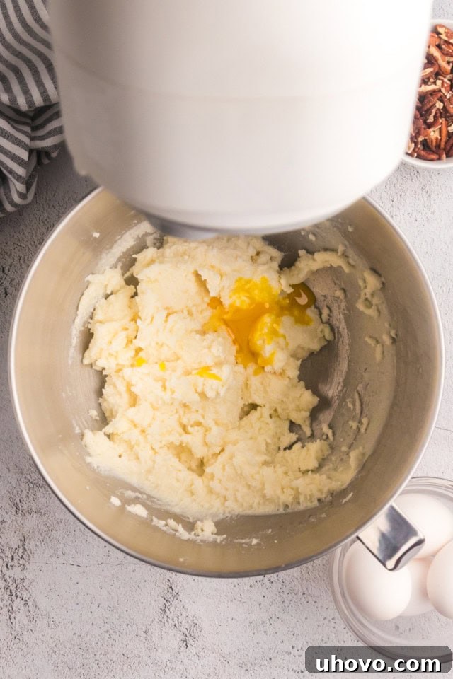 Close-up overhead view of an egg yolk being incorporated into the creamed butter and sugar mixture in a mixing bowl.