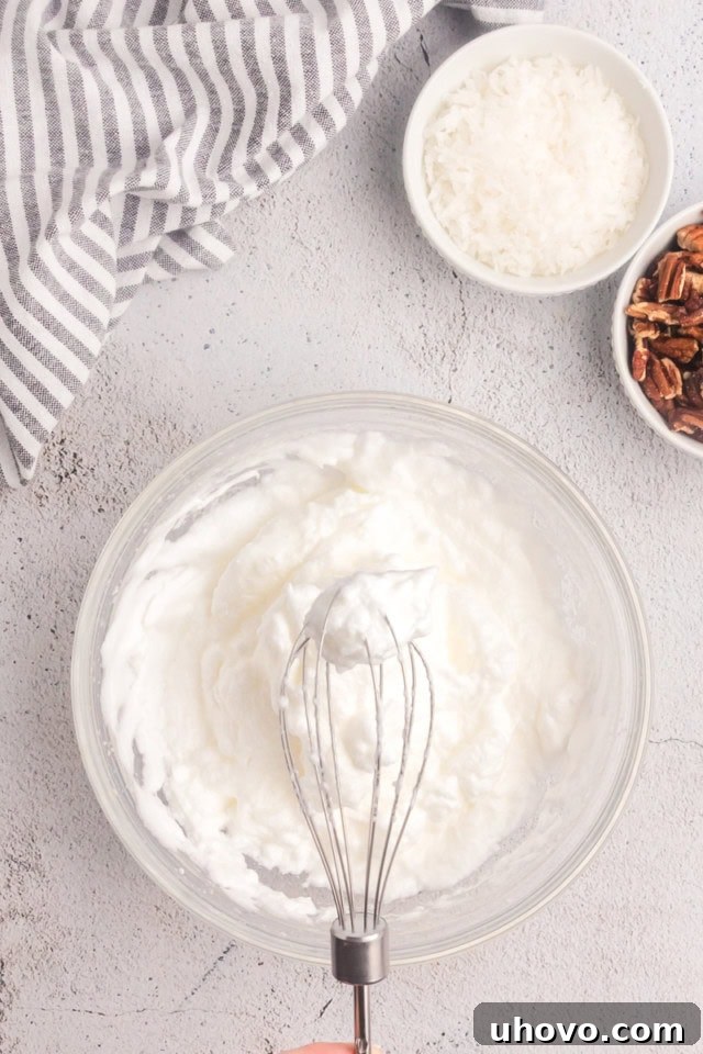 Overhead view of perfectly whipped egg whites forming stiff peaks in a clear glass bowl, indicating readiness for folding into cake batter.