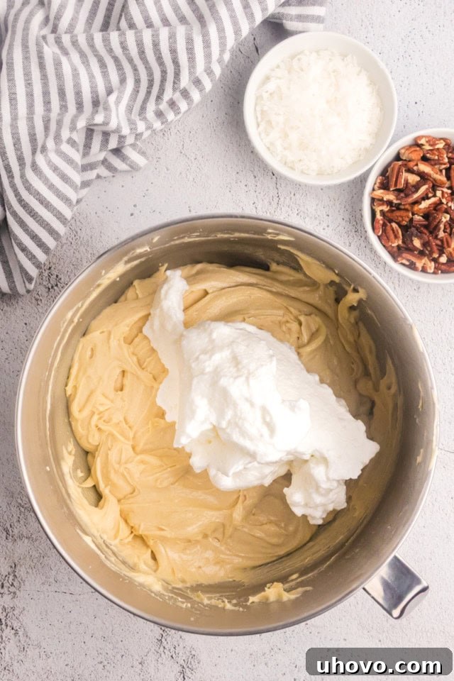 Overhead view of whipped egg whites being gently folded into Italian cream cake batter in a large mixing bowl.
