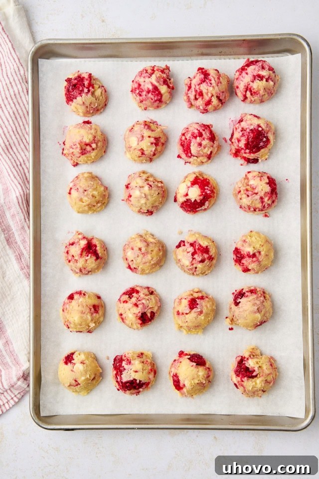 overhead view of scooped raspberry white chocolate cookie dough on a parchment-lined baking sheet