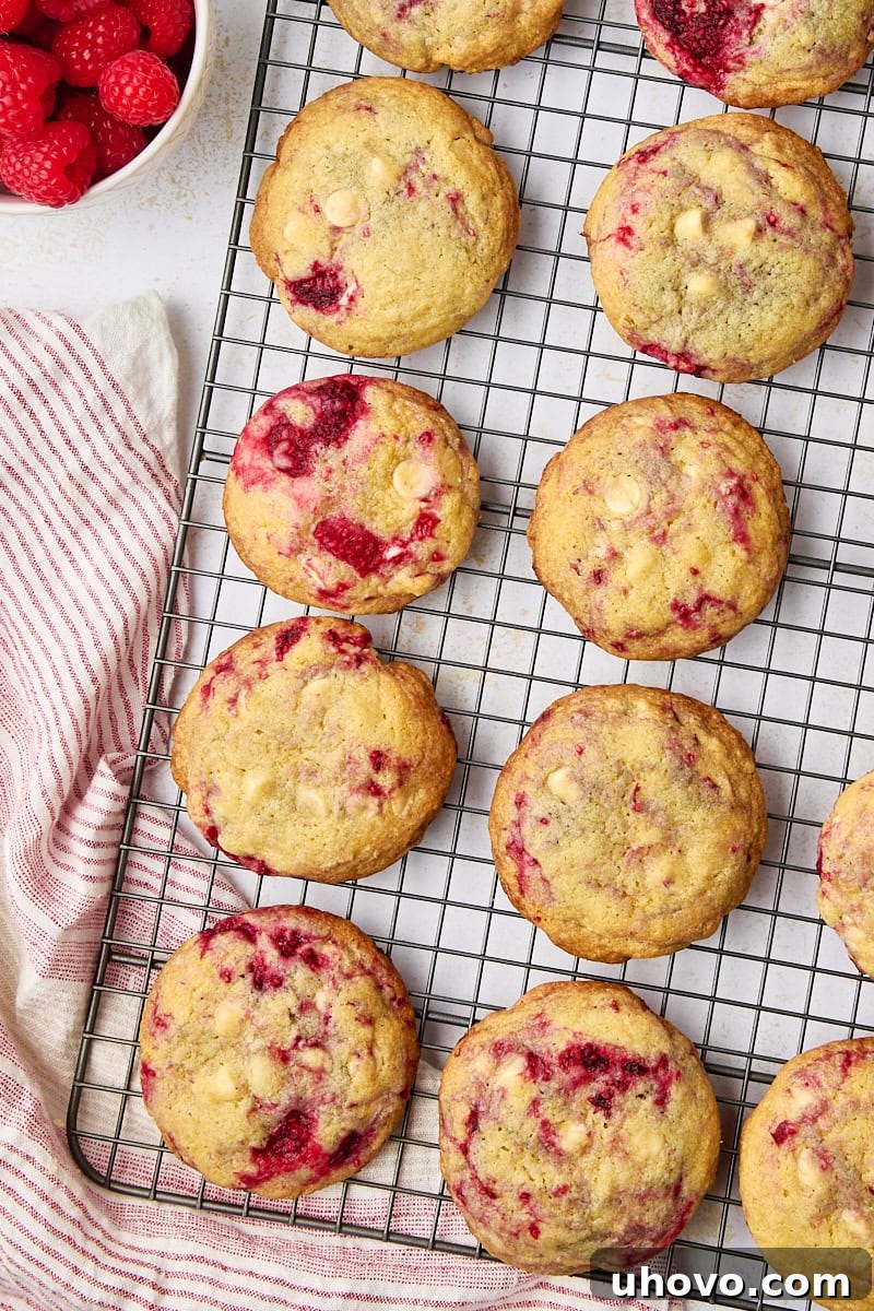 overhead view of raspberry white chocolate cookies cooling on a wire rack; a bowl of raspberries is partially visible to the side