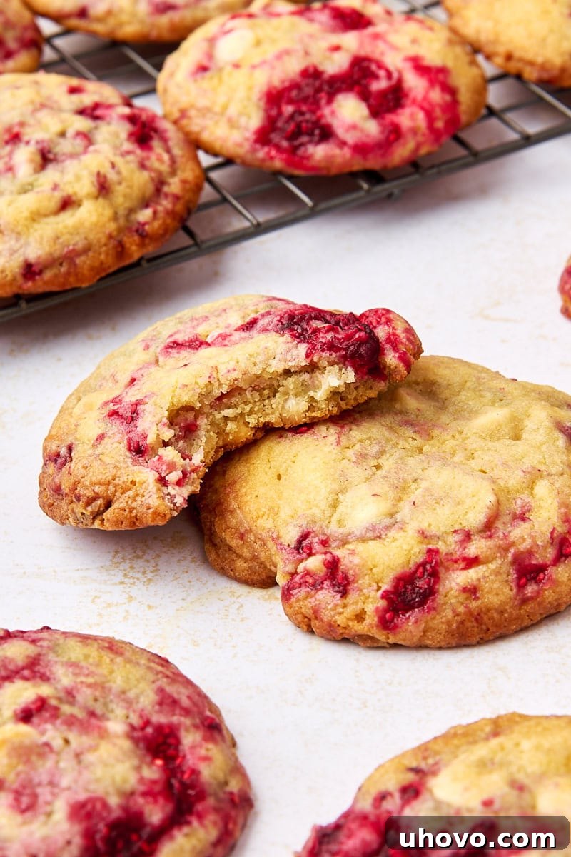 a raspberry white chocolate cookie with a bite missing, partially on top of another cookie; more cookies surrounding and in the background