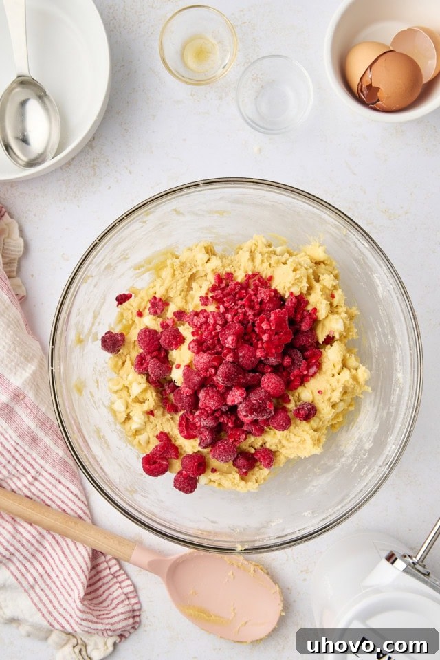 overhead view of frozen raspberries added to cookie dough in a glass mixing bowl