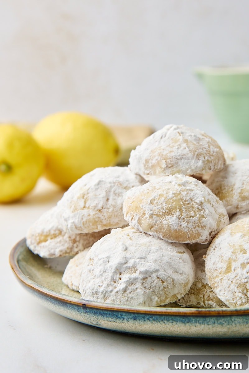 A delightful arrangement of lemon cooler cookies on a green plate, with two vibrant yellow lemons peeking into the frame in the background, emphasizing the fresh citrus flavor.