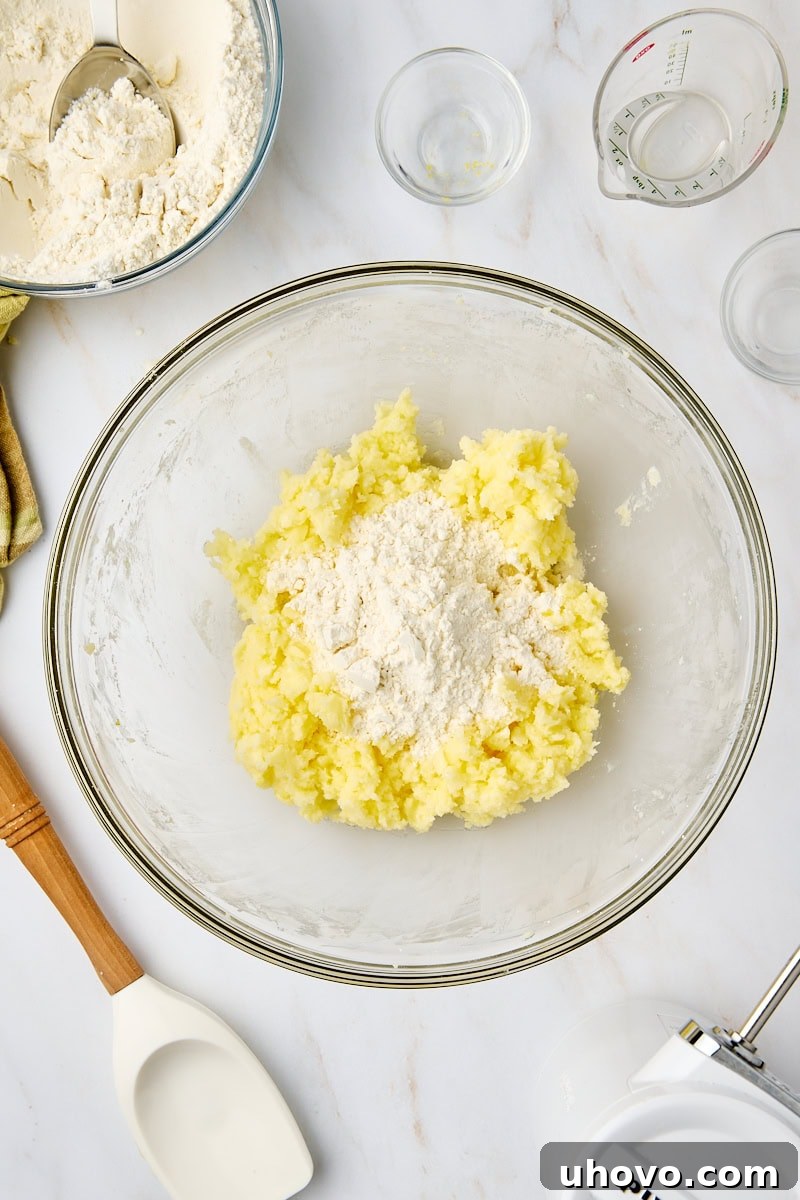 An overhead view capturing the moment dry ingredients are gently folded into the wet mixture, forming the cookie dough for lemon cooler cookies.