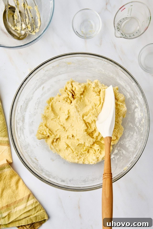 A mixed batch of vibrant lemon cooler cookie dough resting in a clear glass mixing bowl, signaling it's ready for chilling.