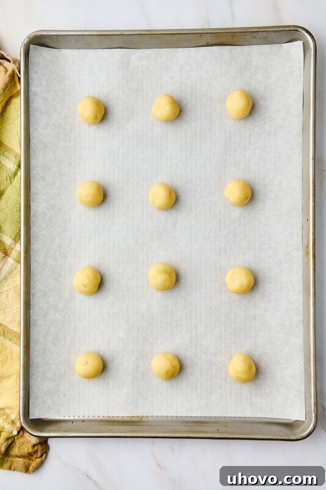 An organized array of portioned lemon cooler cookie dough balls neatly arranged on a parchment-lined baking sheet, prepared for baking.