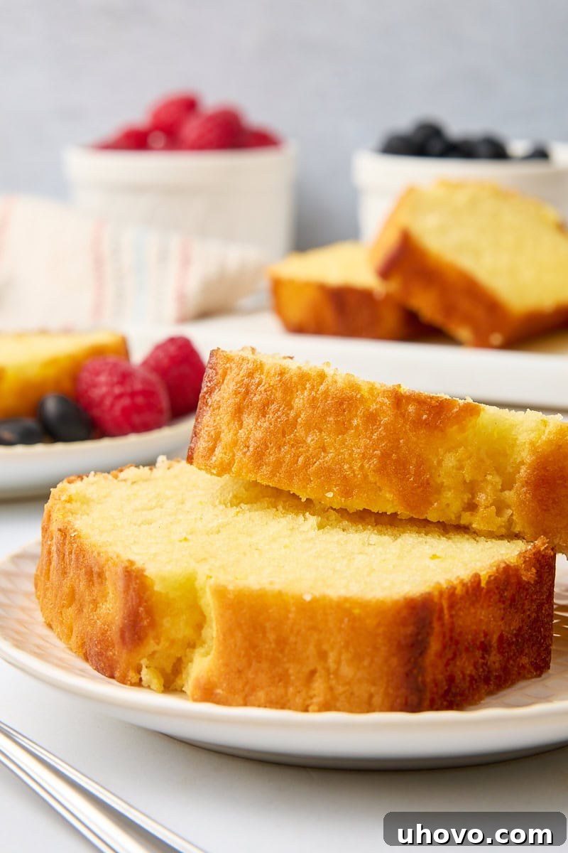 Two perfect slices of orange yogurt cake artfully arranged on a plate, with the rest of the cake and bowls of fresh berries in the softly blurred background, inviting a delicious tasting.