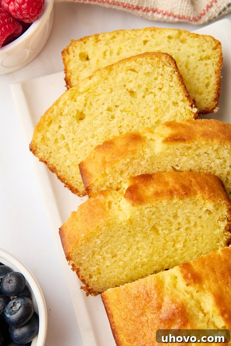 Four golden slices of tender yogurt cake fanned out elegantly beside the remaining loaf, accompanied by small bowls of fresh, vibrant berries, creating an inviting display.