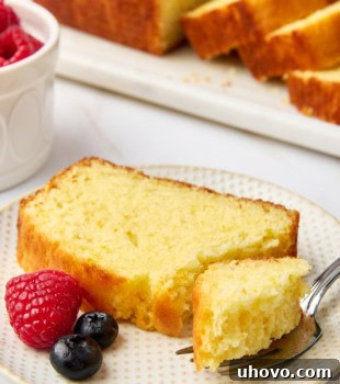 A delicious slice of moist orange yogurt cake on a plate with a bite on a fork; more cake and fresh berries partially visible in the background, ready to be enjoyed.