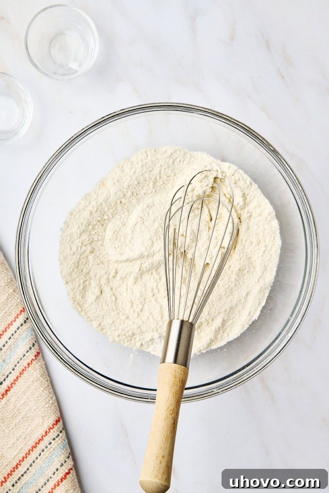 An overhead view of combined dry ingredients for yogurt cake in a glass mixing bowl with a whisk resting inside the bowl, showcasing the simplicity of the first step.