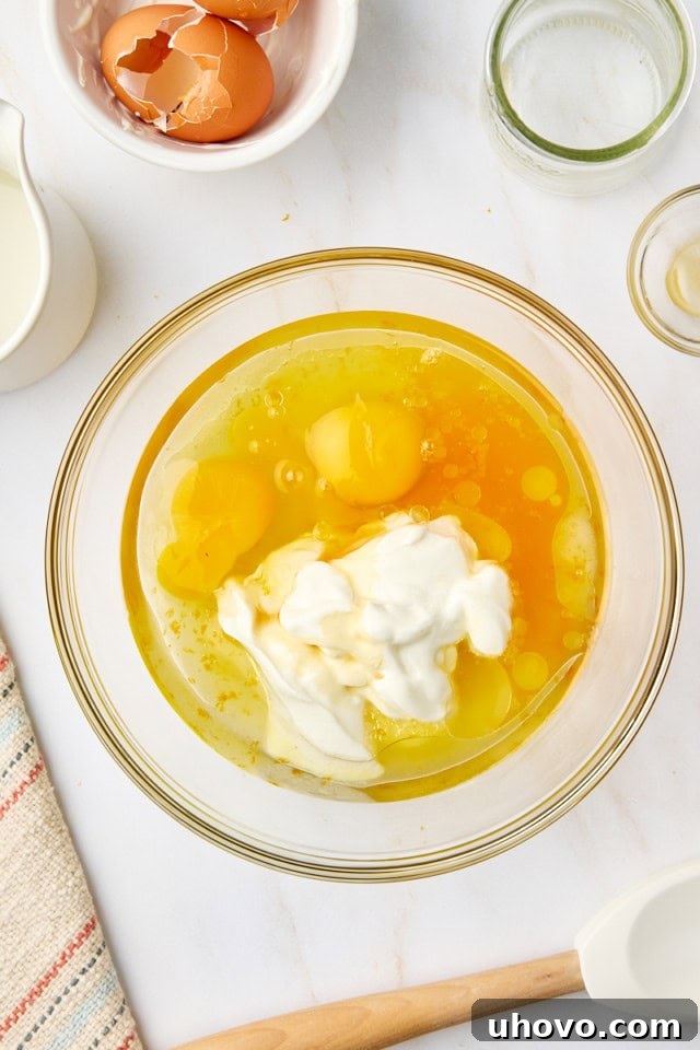 An overhead view of the combined wet ingredients for yogurt cake—Greek yogurt, oil, eggs, orange juice, and vanilla—in a glass mixing bowl, perfectly smooth and ready for the next step.