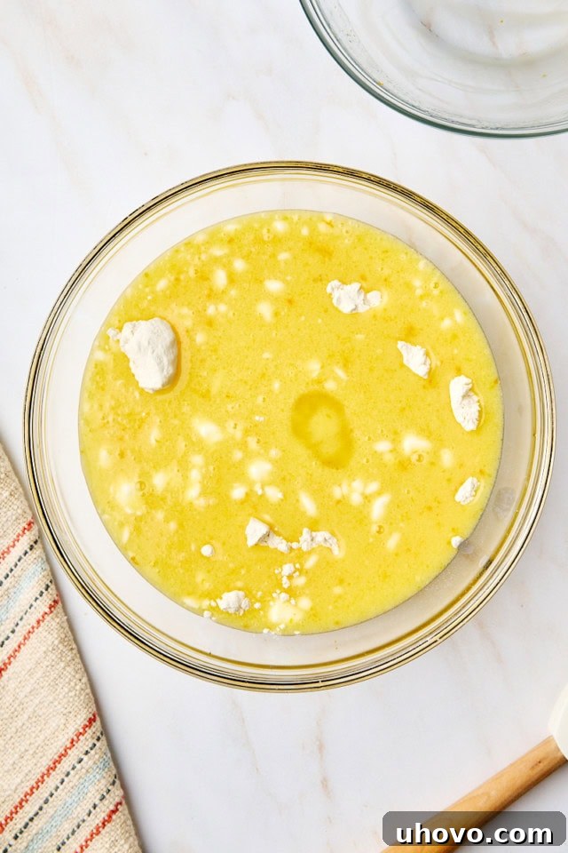 An overhead view of wet ingredients being carefully added to the dry ingredients for yogurt cake in a glass mixing bowl, illustrating the gentle combining process.