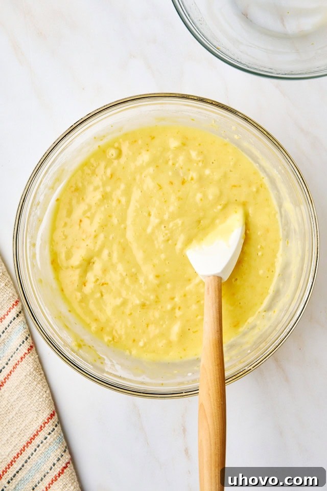 An overhead view of perfectly mixed yogurt cake batter in a glass mixing bowl, with a rubber spatula resting gently in the bowl, showing the ideal consistency before baking.