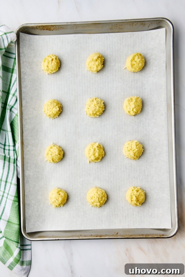 Overhead view of perfectly portioned coconut lime cookie dough balls arranged on a parchment-lined baking sheet, ready for the oven.
