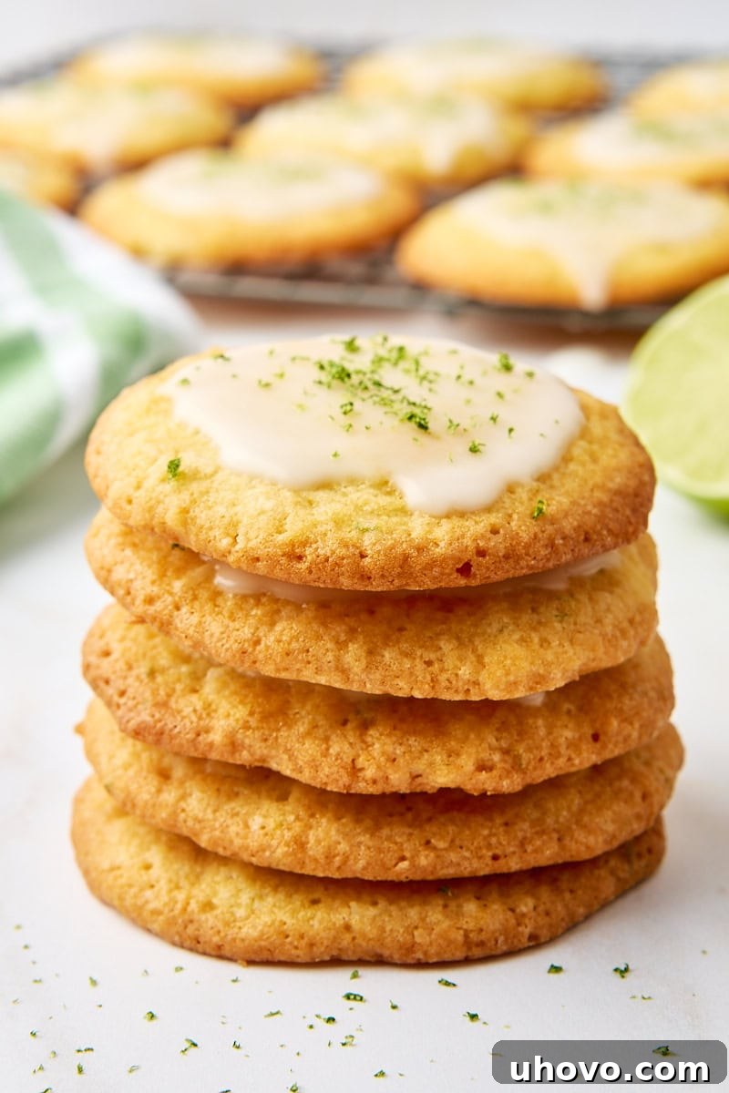 A stack of five perfectly baked coconut lime cookies with a tangy lime glaze, with more cookies and a slice of lime in the blurred background.