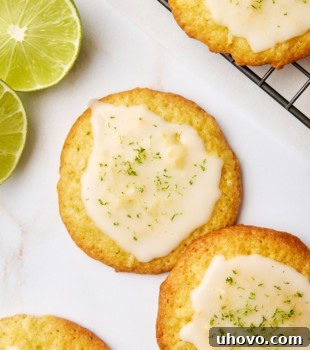 Overhead view of two coconut lime cookies on a white surface, adorned with more cookies and fresh lime slices in the background.