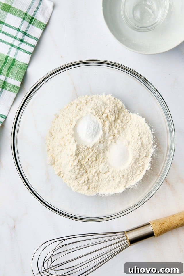 Overhead view of flour, baking soda, and salt measured in a glass mixing bowl, ready to be combined for the cookie dough.