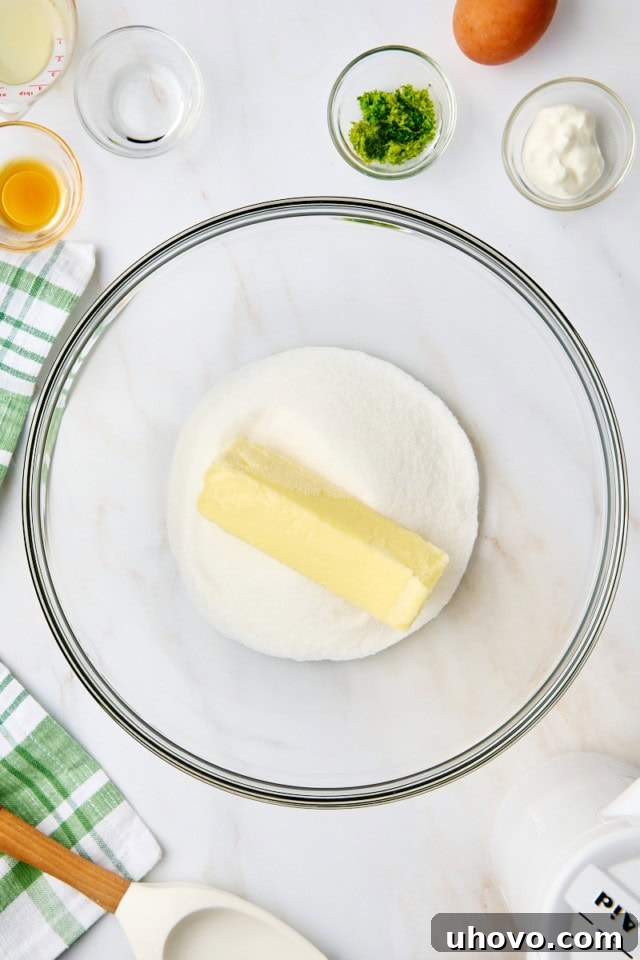 Overhead view of softened butter and granulated sugar being creamed together in a glass mixing bowl until light and fluffy.