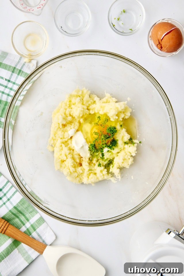 Overhead view of sour cream, an egg, lime zest, lime juice, vanilla extract, and coconut extract being added to the creamed butter and sugar mixture in a glass mixing bowl.