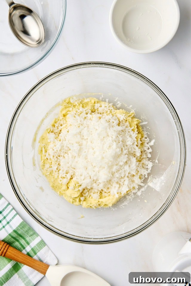 Overhead view of the dry flour mixture being gradually added to the wet ingredients for coconut lime cookies in a glass mixing bowl.