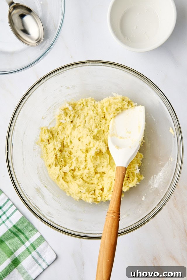 Overhead view of the fully mixed coconut lime cookie dough in a glass mixing bowl, showing its thick and textured consistency.