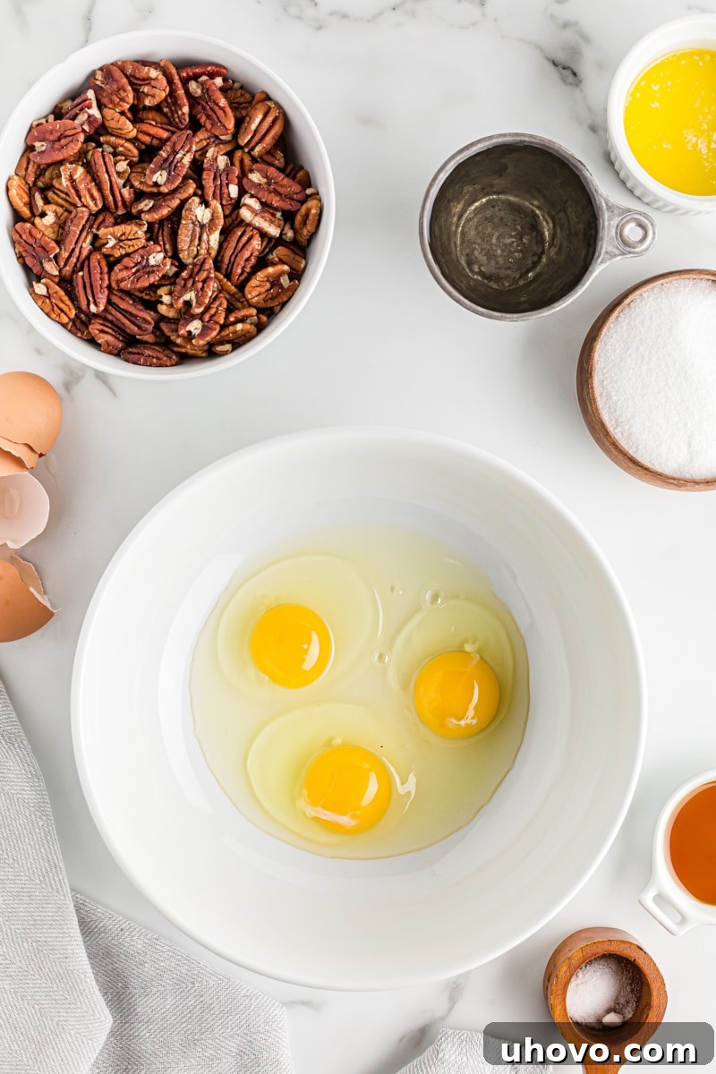 Overhead view of three large eggs cracked into a mixing bowl, ready to be beaten for the pecan pie filling.