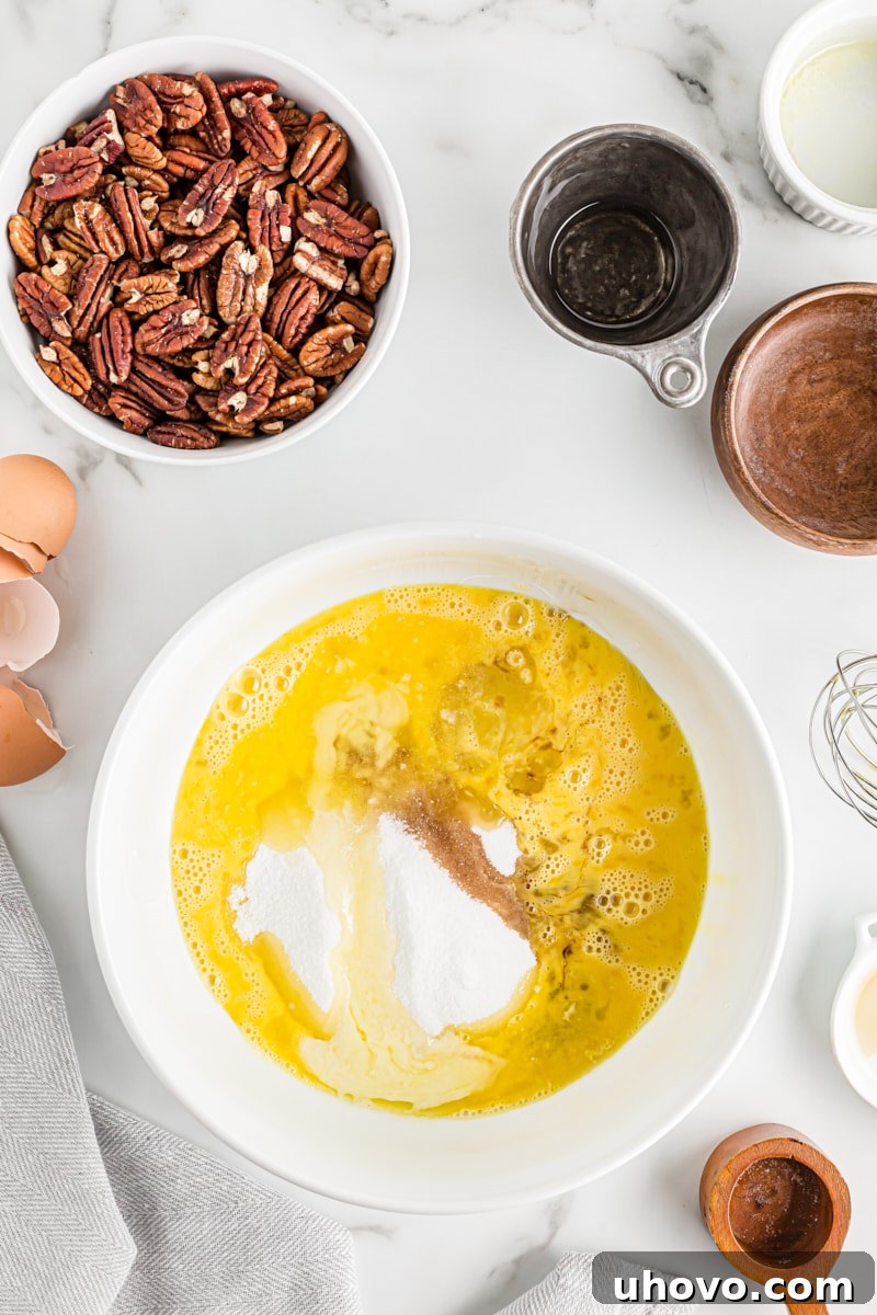 Overhead view of a mixing bowl containing the initial pecan pie filling ingredients: beaten eggs, corn syrup, granulated sugar, melted butter, vanilla extract, and salt, before they are mixed together.