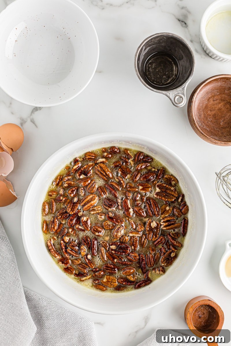 Overhead view of a bowl of pecan pie filling, with pecan halves gently stirred into the rich, amber mixture.