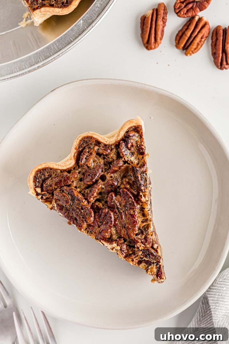 Overhead view of a perfect slice of classic pecan pie on a white plate, showcasing its golden crust and rich, pecan-filled gooey center.