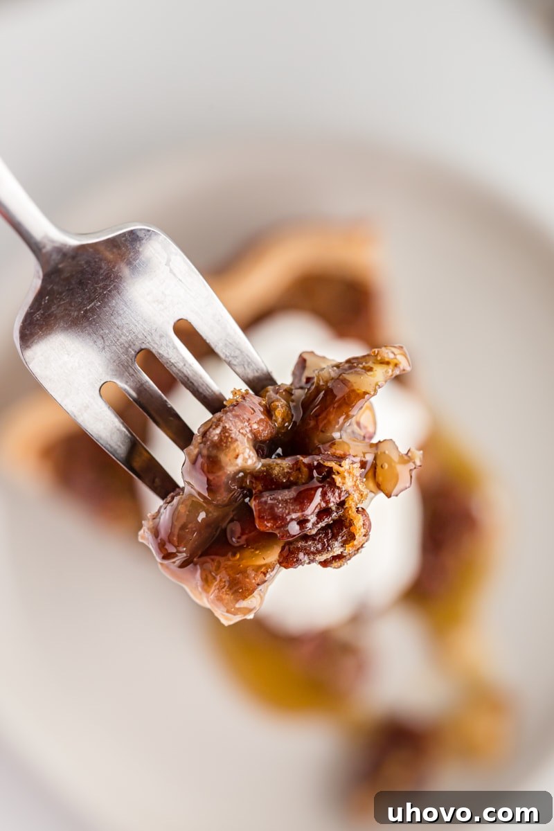 Close-up view of a fork taking a bite from a slice of classic pecan pie, highlighting the gooey filling and crunchy pecans.
