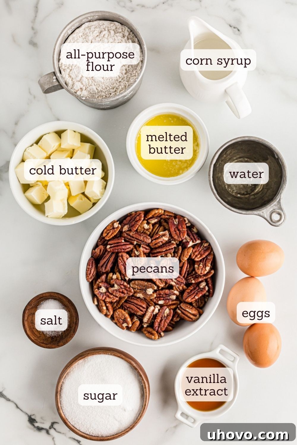 An overhead shot showcasing all the essential ingredients laid out for making a classic pecan pie: flour, sugar, butter, eggs, corn syrup, vanilla, salt, and a generous pile of pecan halves, ready to be transformed into a delicious dessert.