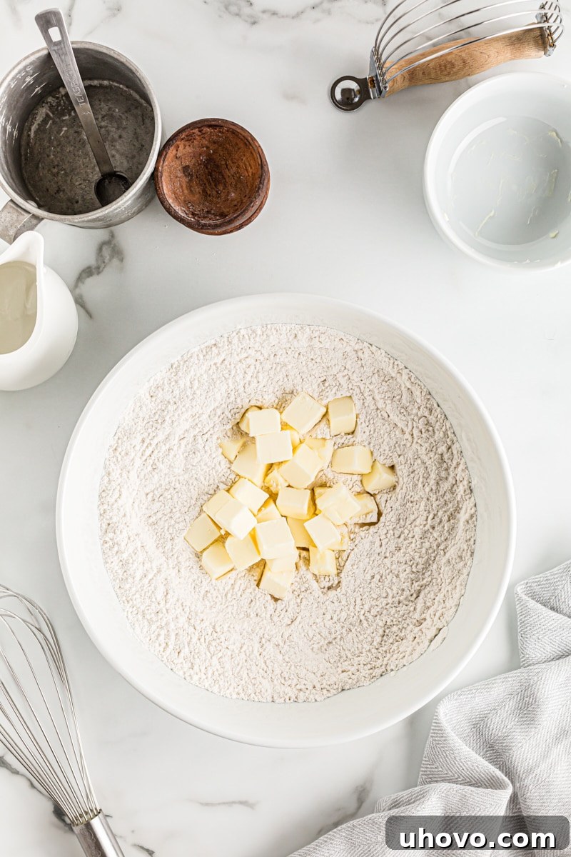 Overhead view of cold butter cubes added to a bowl containing dry pie crust ingredients, ready for mixing.