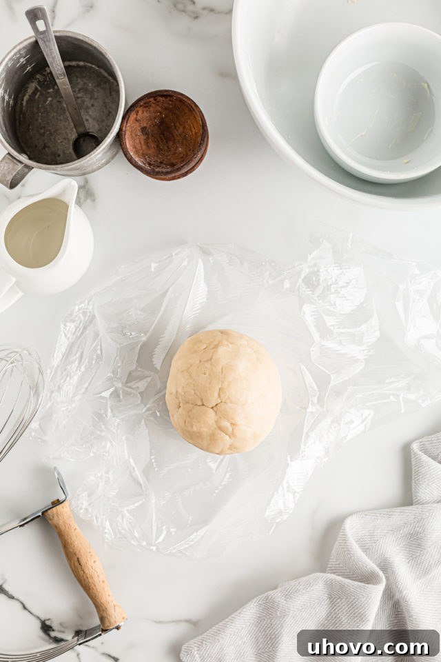 Overhead view of a prepared pie dough ball tightly wrapped in plastic wrap, ready for refrigeration.