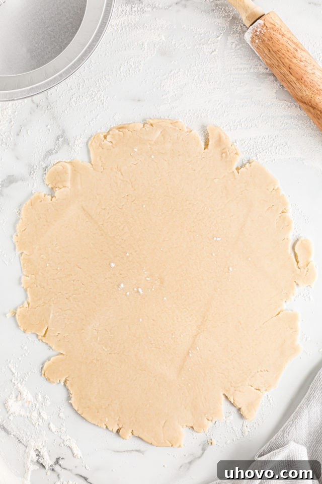 Overhead view of homemade pie crust dough rolled out into a rough circular shape on a lightly floured surface.