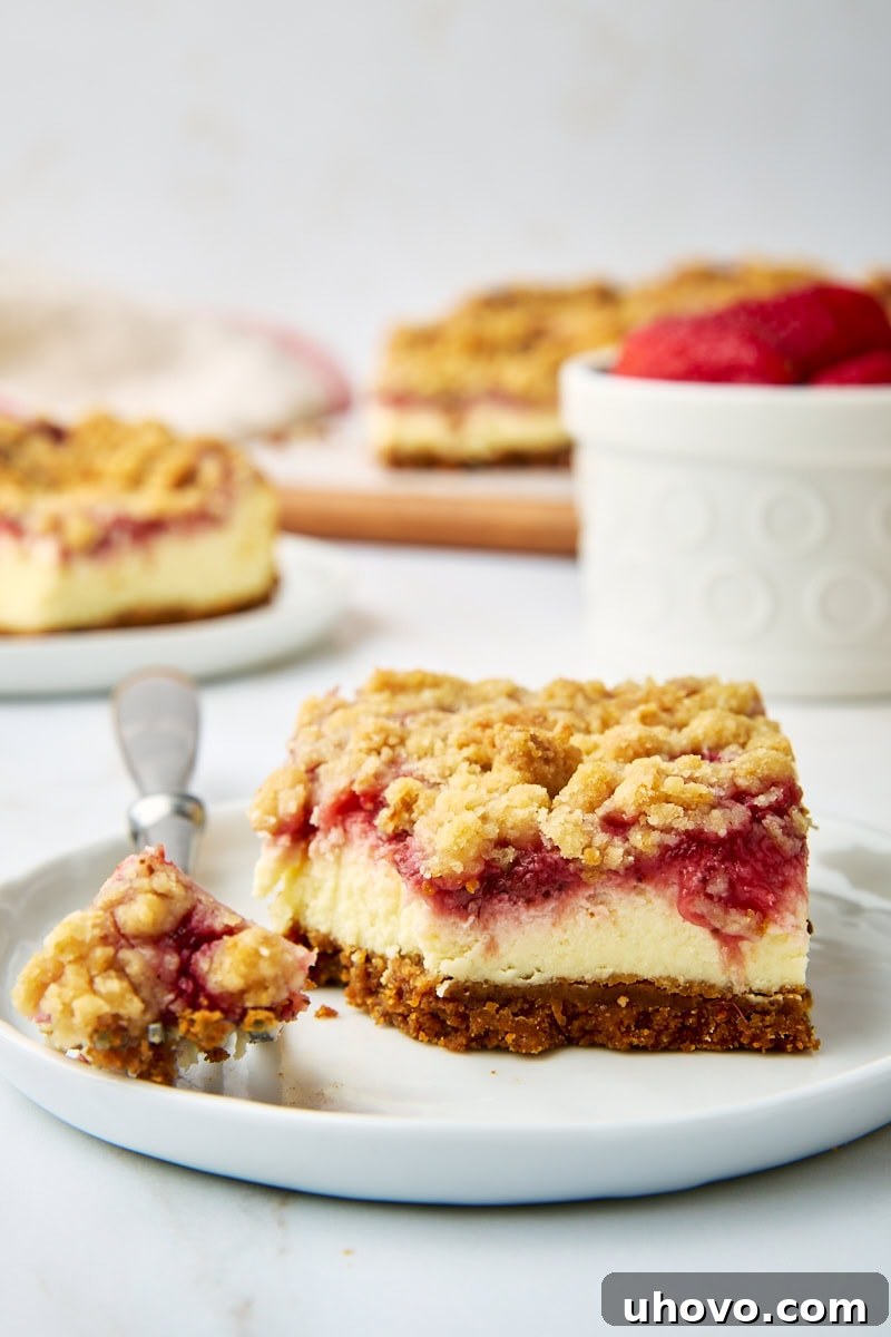 A perfectly portioned strawberry cheesecake bar on a pristine white plate, with a fork gently taking a bite. In the softly blurred background, more delectable bars are visible alongside a bowl of fresh, vibrant strawberries, hinting at the deliciousness to come.